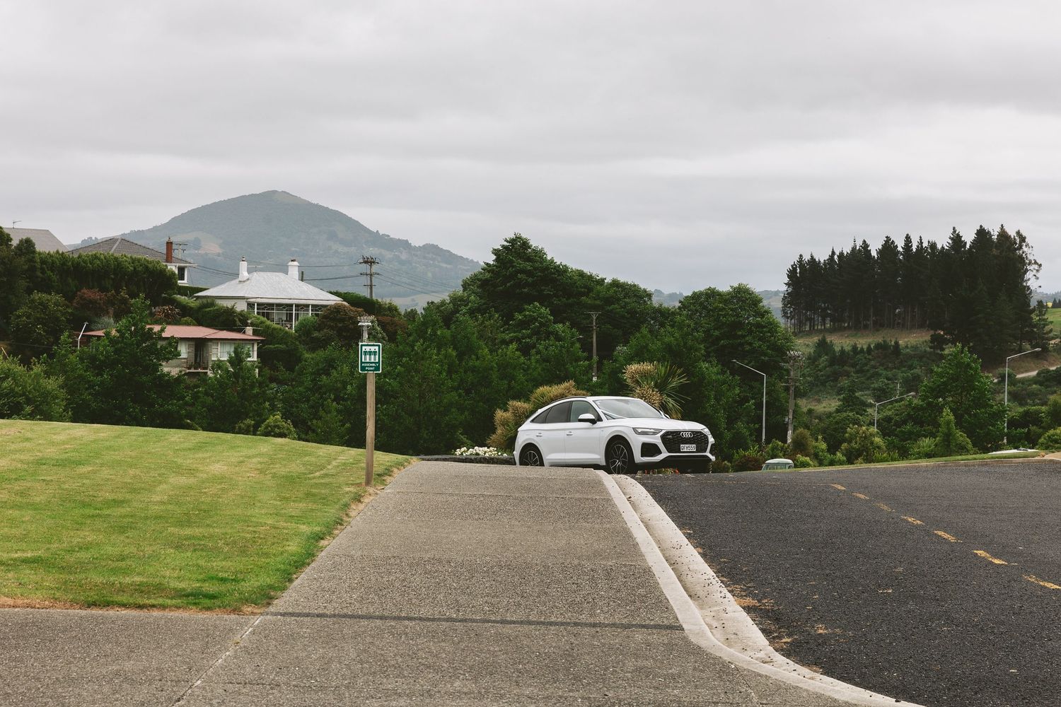 White luxury car parked on a hilltop road with green mountains in the background.