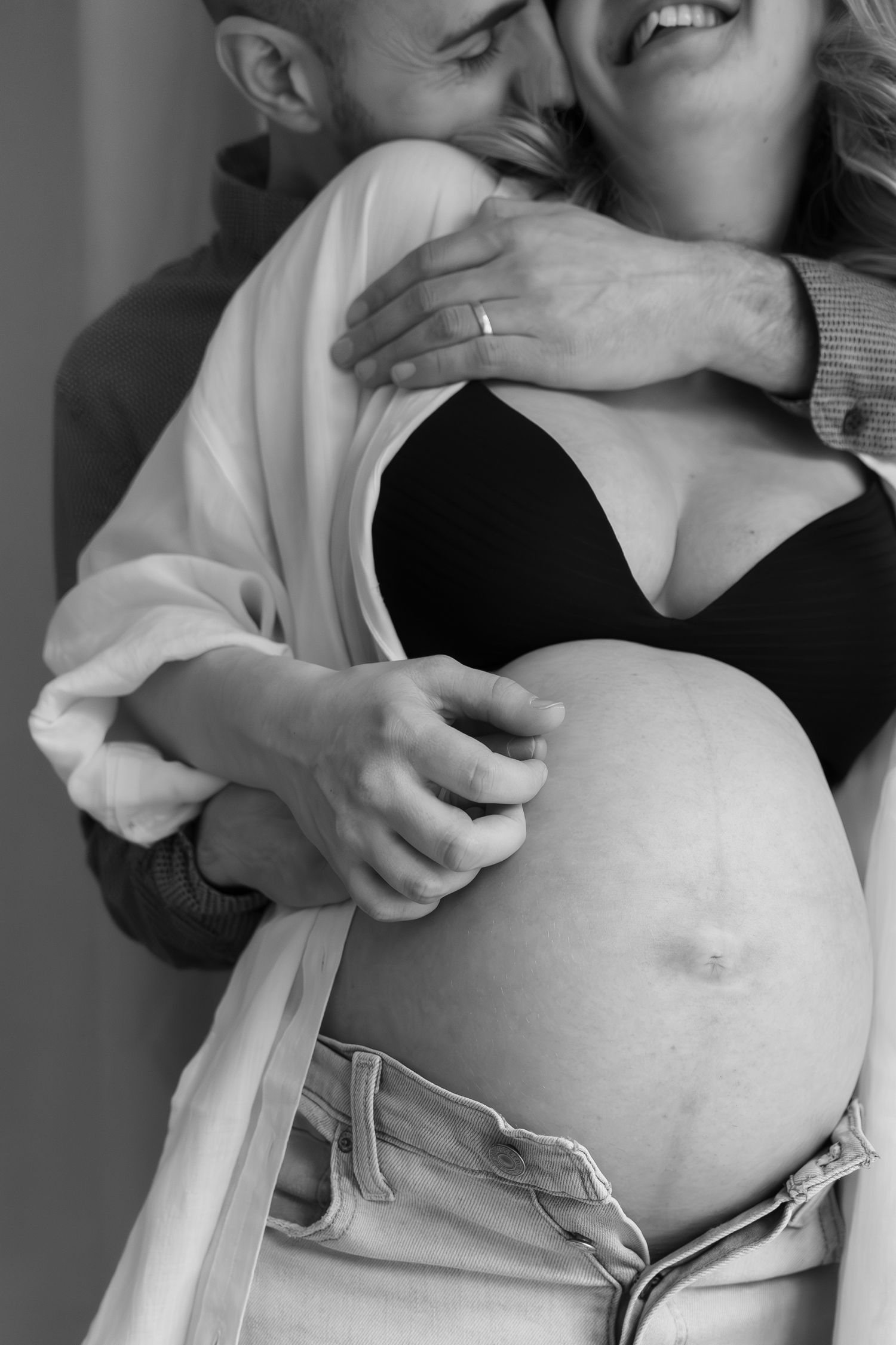 Black and white intimate maternity photo showing couple embracing with hands tenderly placed on pregnant belly.