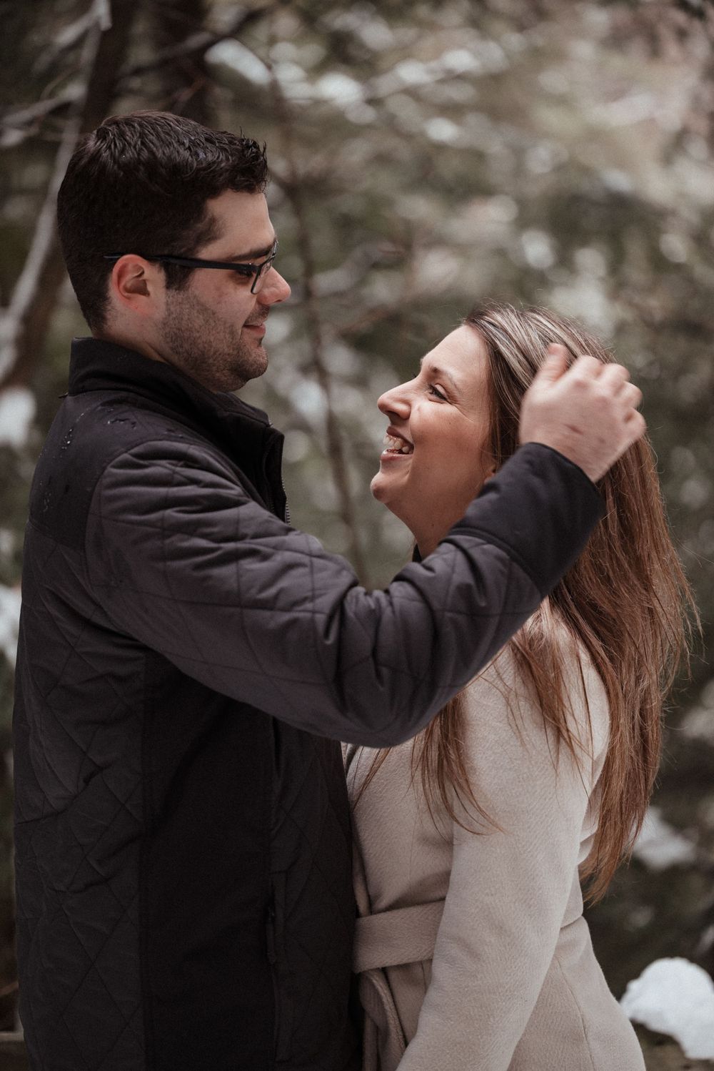 Candid moment of affection between a couple during a winter forest photoshoot.
