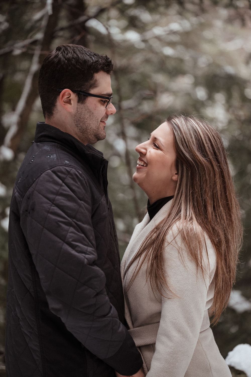 Joyful couple sharing a laugh during their winter forest engagement session.