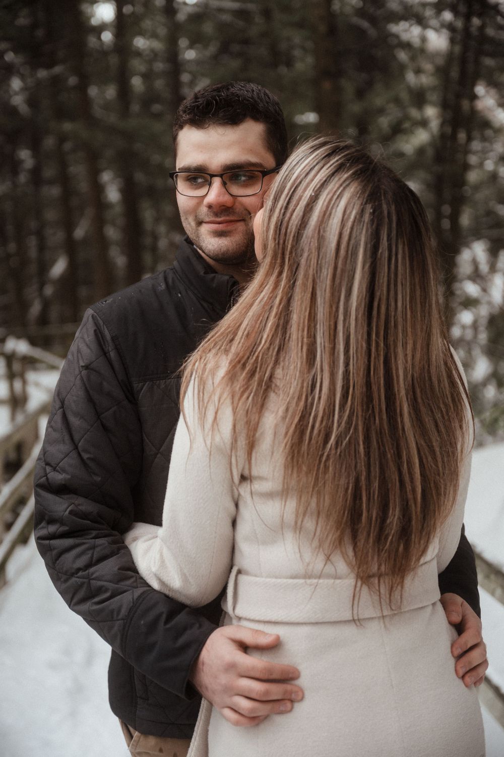 Intimate winter portrait of a couple embracing on a snowy forest path.