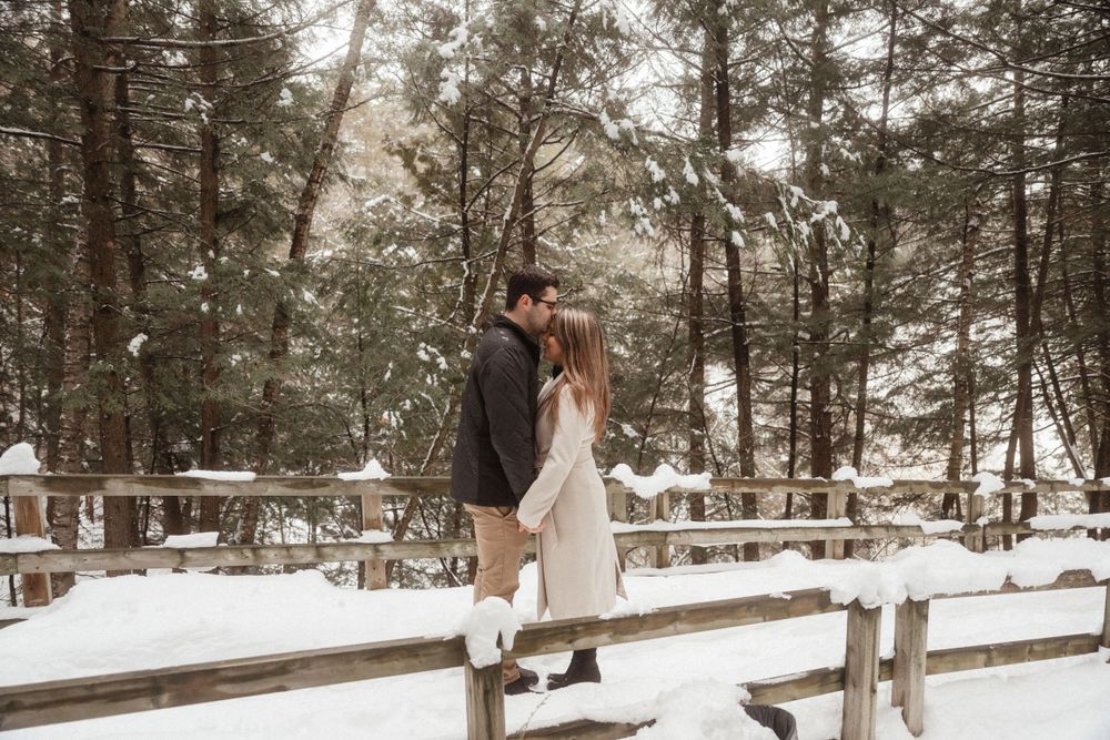 Couple standing on a wooden fence in a magical winter forest setting.