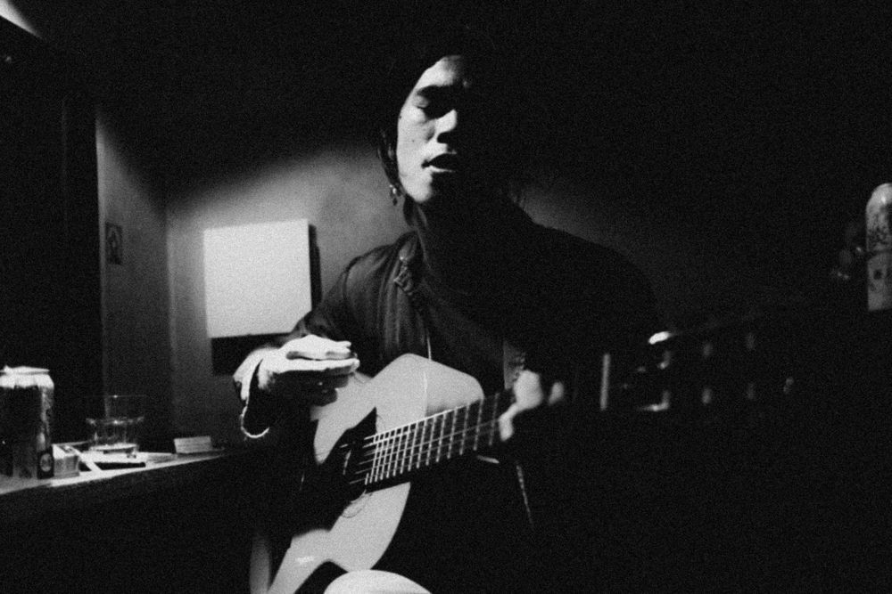 Black and white photo of someone playing acoustic guitar in a dimly lit room.