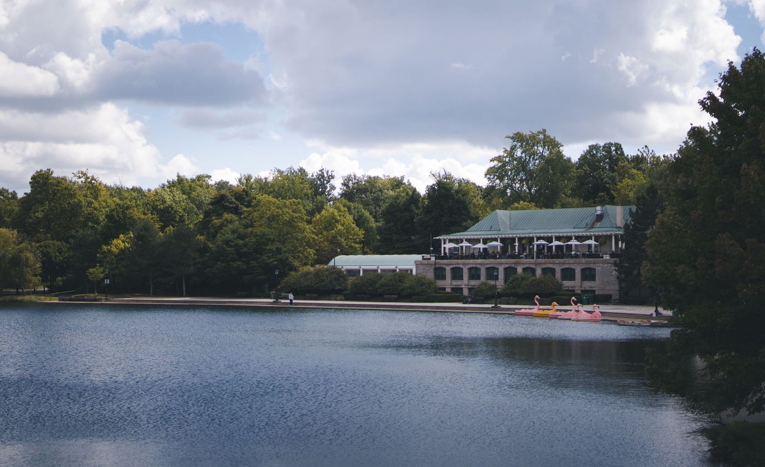 White lakeside building with boats docked along the shoreline on a cloudy summer day.