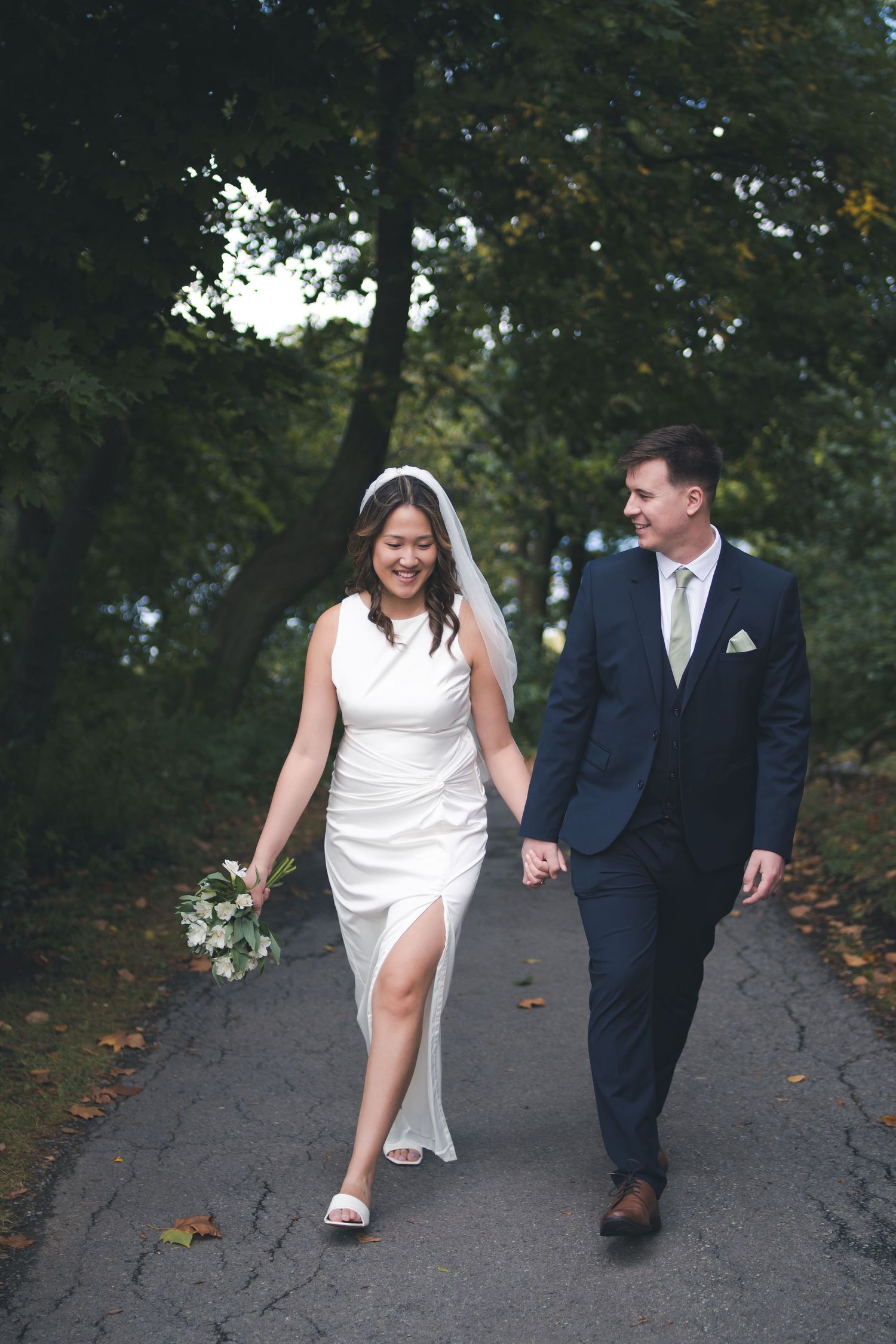 Wedding couple walking together on path surrounded by autumn trees.