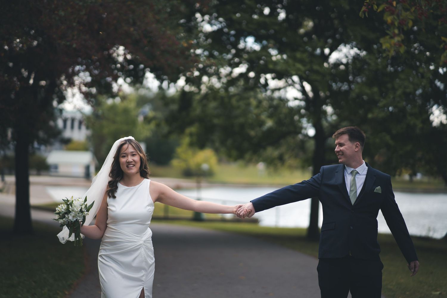 Wedding couple enjoying playful moment on outdoor path near water.