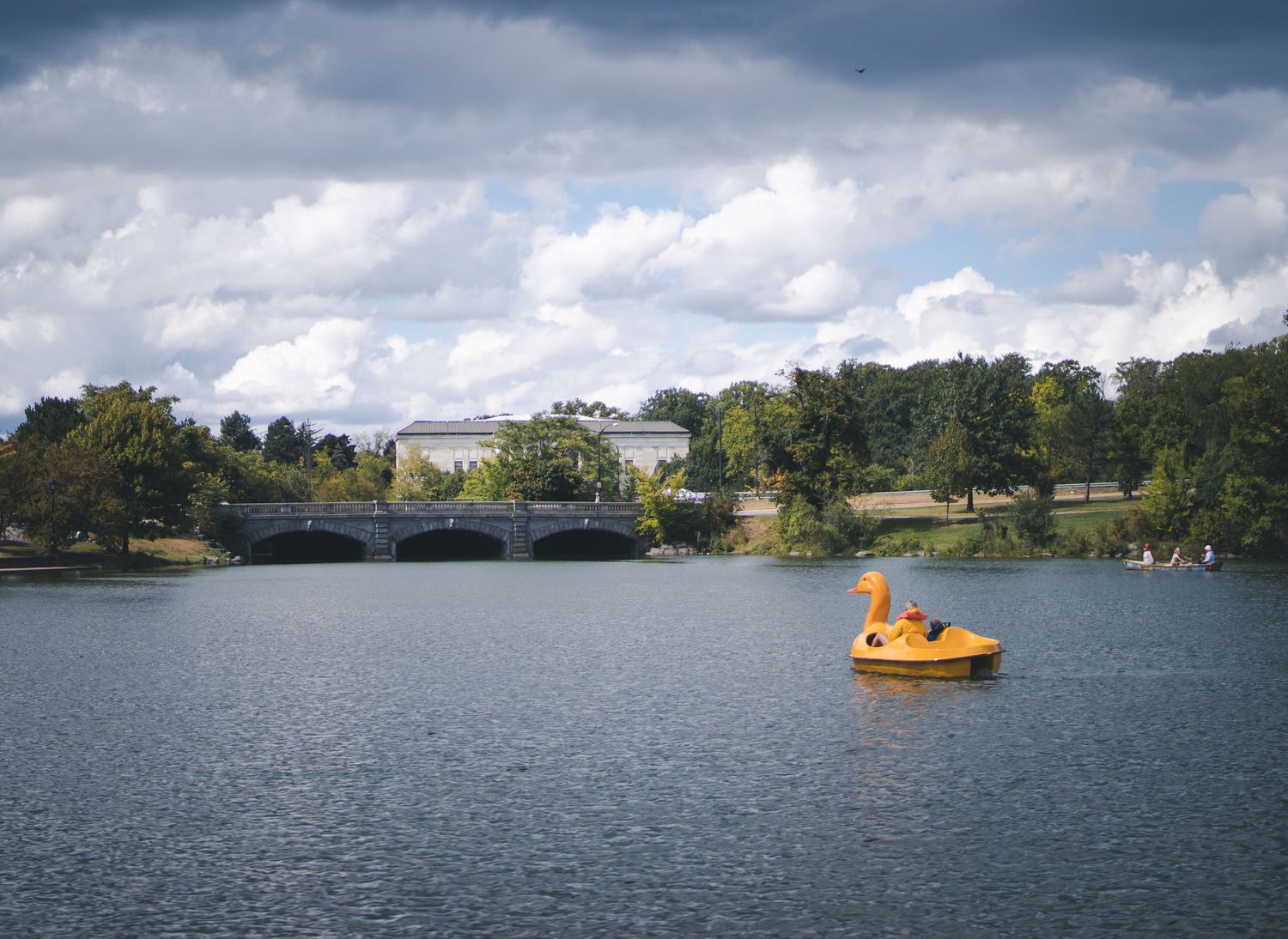 Yellow paddleboat on a lake with buildings and trees visible on the distant shore.