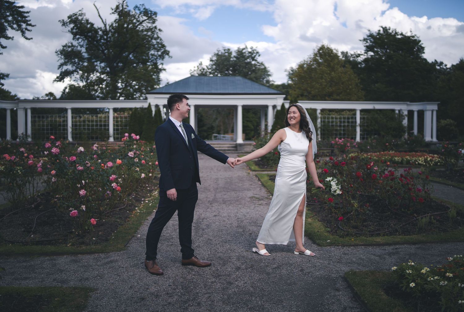 Wedding couple posing in romantic rose garden with white gazebo and trellis.