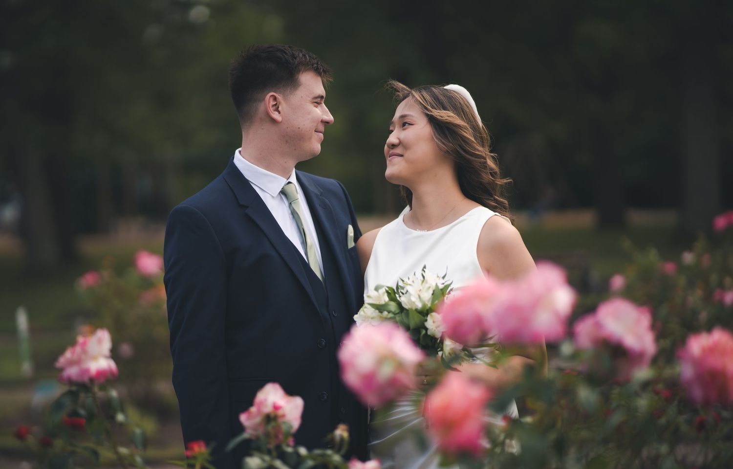 Elegant wedding photo taken in garden with pink roses framing the couple.