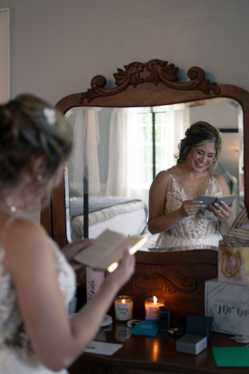 A reflection in an antique mirror shows someone in a wedding dress looking at their phone by candlelight.