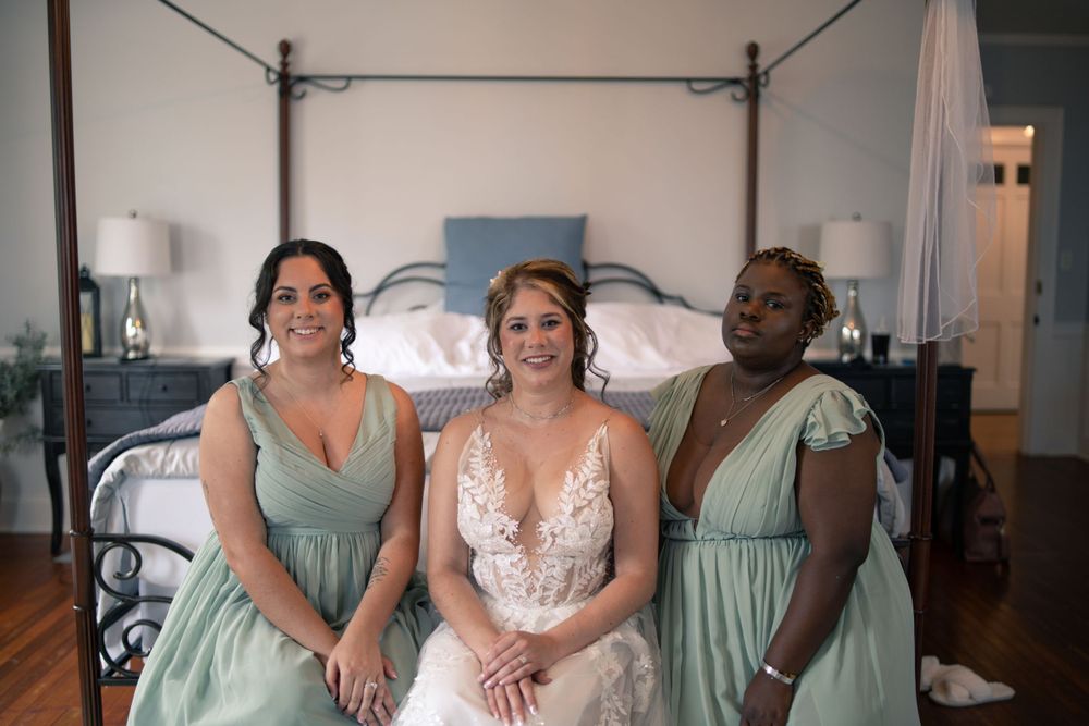 Wedding party seated on bed wearing sage green bridesmaid dresses.