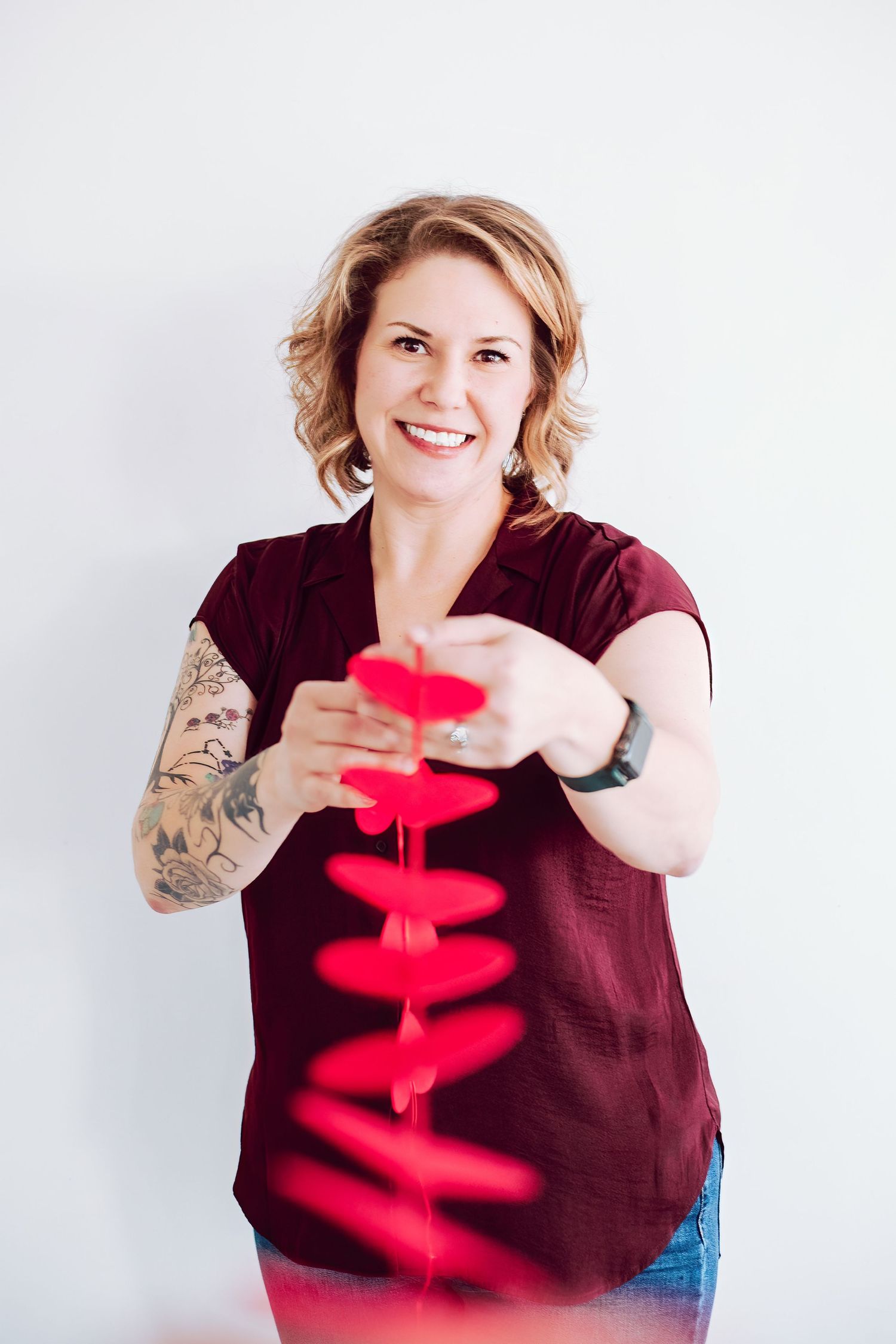 Photographer in burgundy shirt holding red heart decorations against white background.