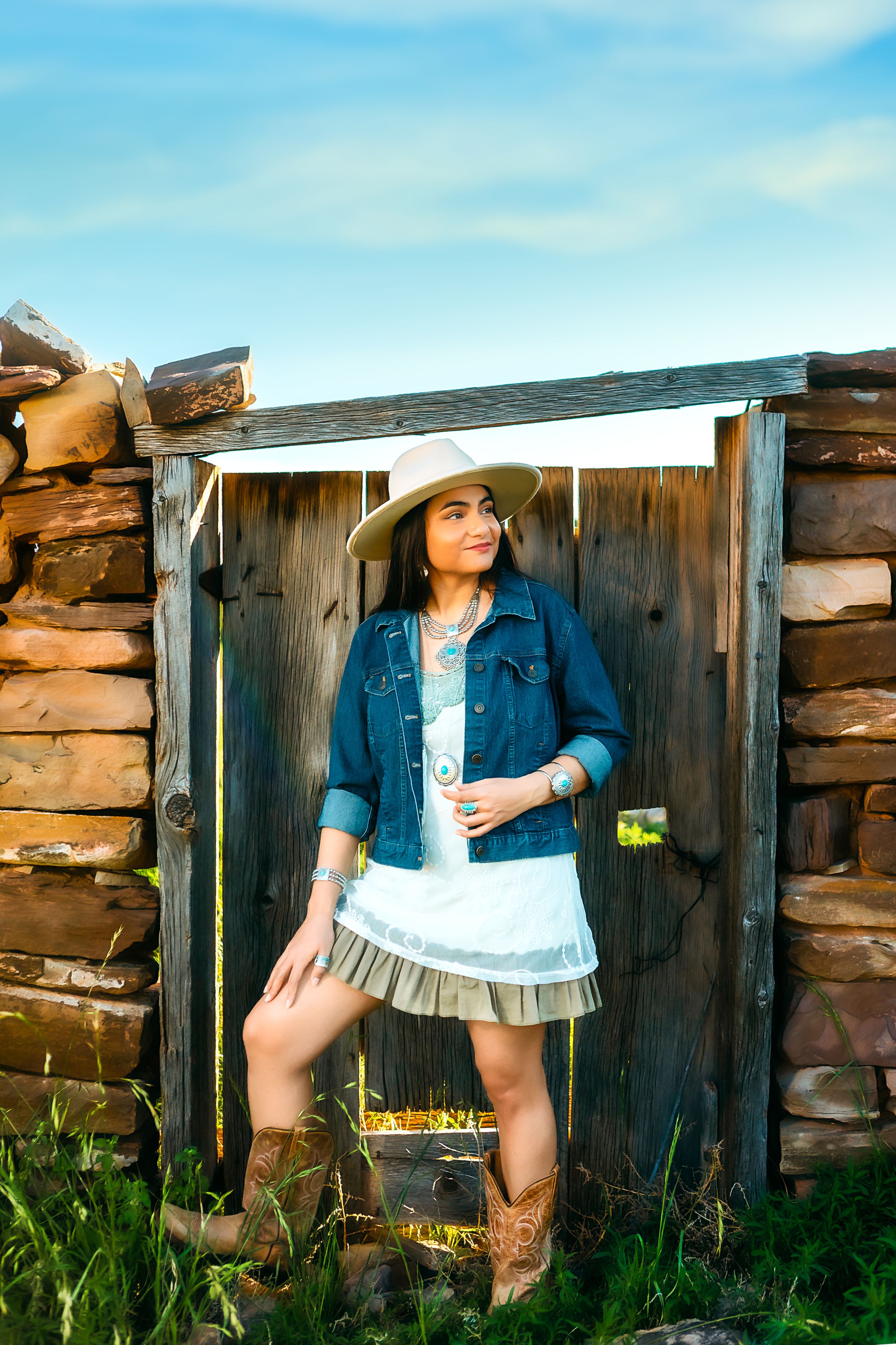 A rustic western style portrait against a stone wall featuring cowboy boots and a denim jacket.