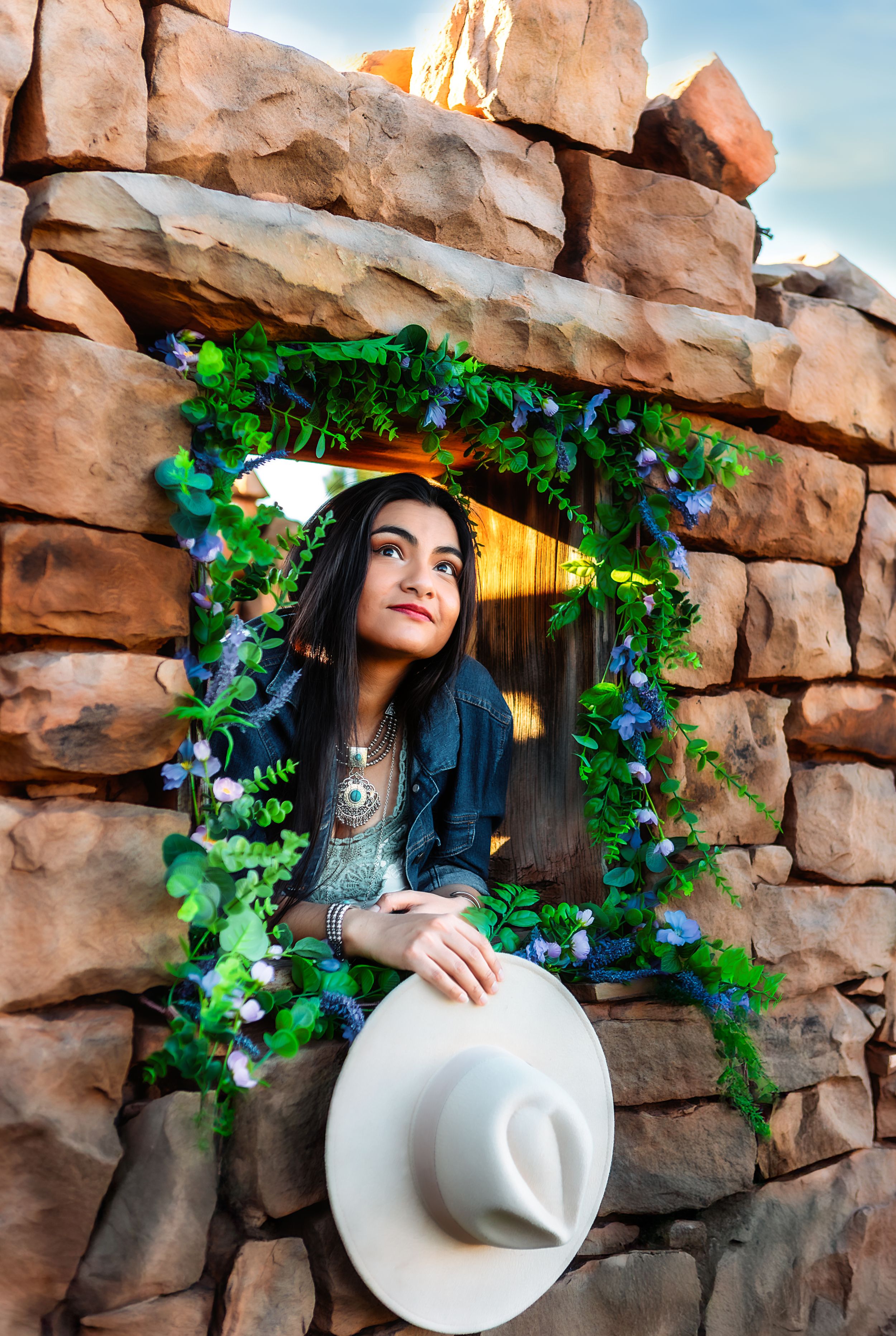Stone archway adorned with green vines and purple flowers frames a white cowboy hat.