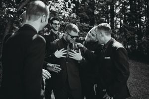 Black and white photo of groomsmen gathered in a circle sharing a lighthearted moment.