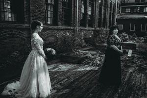 Black and white photo of two figures in formal attire standing in an industrial courtyard.