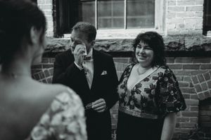 A casual moment between wedding guests captured in black and white against a brick wall backdrop.