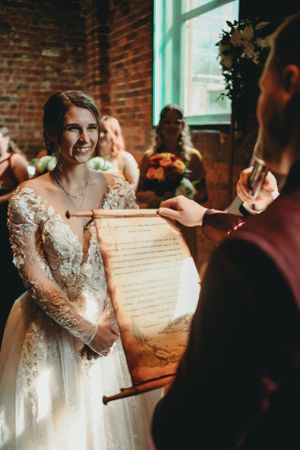 A bride in a lace wedding dress smiles during the ceremony in a rustic brick venue.