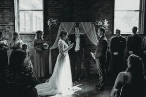 Wedding ceremony captured in black and white showing silhouettes against a window in an industrial space.
