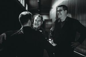 Three people share a lighthearted conversation in a black and white candid moment.