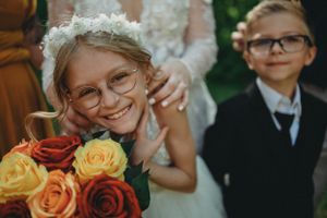 Young attendee with glasses smiles brightly while holding colorful roses at a wedding.