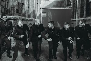 Groomsmen in dark suits pose playfully in an industrial alleyway setting with brick walls.