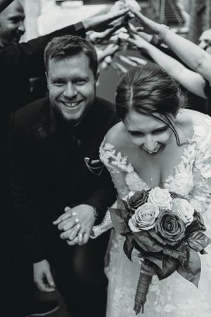 Black and white candid moment of newlyweds walking under raised arms during wedding exit.