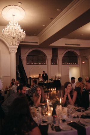 Elegant wedding reception venue with crystal chandelier and candlelit tables filled with guests.