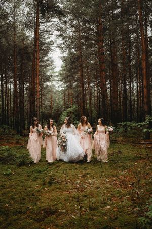 Bridal party in pink dresses poses together in tall pine forest.