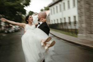 A joyful wedding couple dances on a rainy street outside their venue.