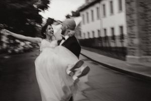 Black and white photo of newlyweds dancing and spinning joyfully outdoors.