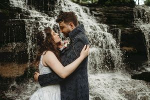 Romantic couple embrace in front of cascading waterfall during wedding photoshoot.
