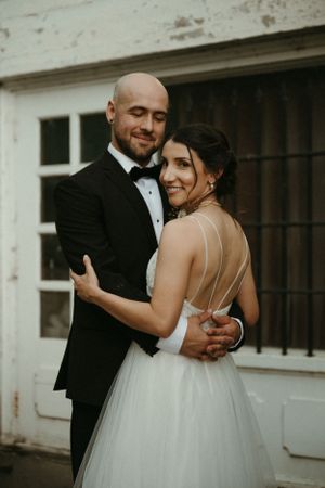 A romantic wedding moment between newlyweds dancing outside a white building.