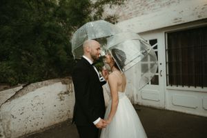 A windy wedding photo with the bride's veil flowing in the breeze against a white building.
