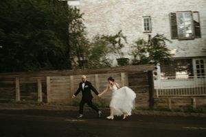 Playful newlyweds running and holding hands on a street at twilight.