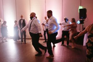 Two guests dance enthusiastically together at a wedding reception in a pink-lit venue.