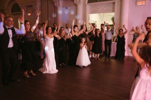 Wedding guests dance and celebrate with raised arms on the dance floor at an indoor reception.