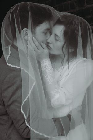 An intimate black and white portrait of newlyweds sharing a tender moment under a delicate veil.