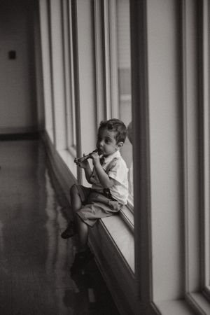Young boy sitting pensively by window in black and white portrait.
