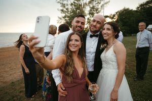 Wedding guests gather for a selfie outdoors at sunset with a couple on their special day.
