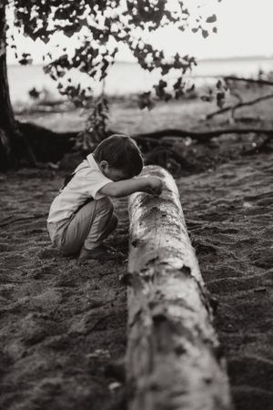 A young child rests on a fallen log in a contemplative black and white nature scene.