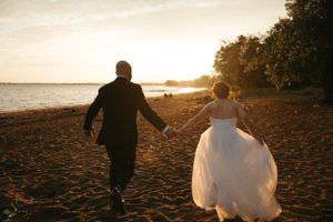 Les jeunes mariés marchant main dans la main sur la plage au coucher du soleil.