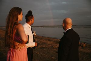 Cérémonie de mariage sur la plage au coucher du soleil avec arc-en-ciel apparaissant en arrière-plan.