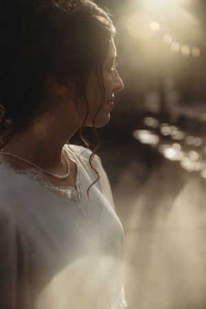 Side profile of a bride in golden sunlight wearing a delicate pearl necklace.