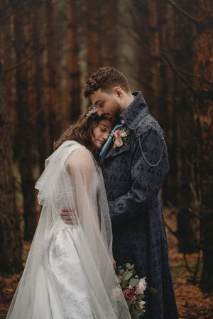 Romantic wedding portrait of couple in autumn forest with bride in flowing white gown.