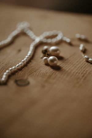 Pearl necklace and jewelry accessories arranged on wooden surface in moody lighting.