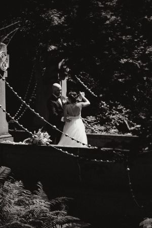 Une photographie romantique en noir et blanc d'un couple sur un pont décoratif entouré de feuillages. Photo intime des mariés.
