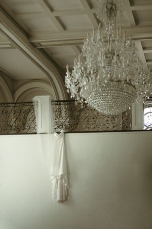 An elegant wedding dress hanging beneath a crystal chandelier in a grand ballroom.