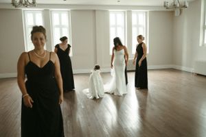 Bridesmaids in elegant black dresses gather around a bride in white in a spacious room.