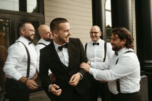 Groomsmen in suspenders and bowties share a candid moment outdoors.